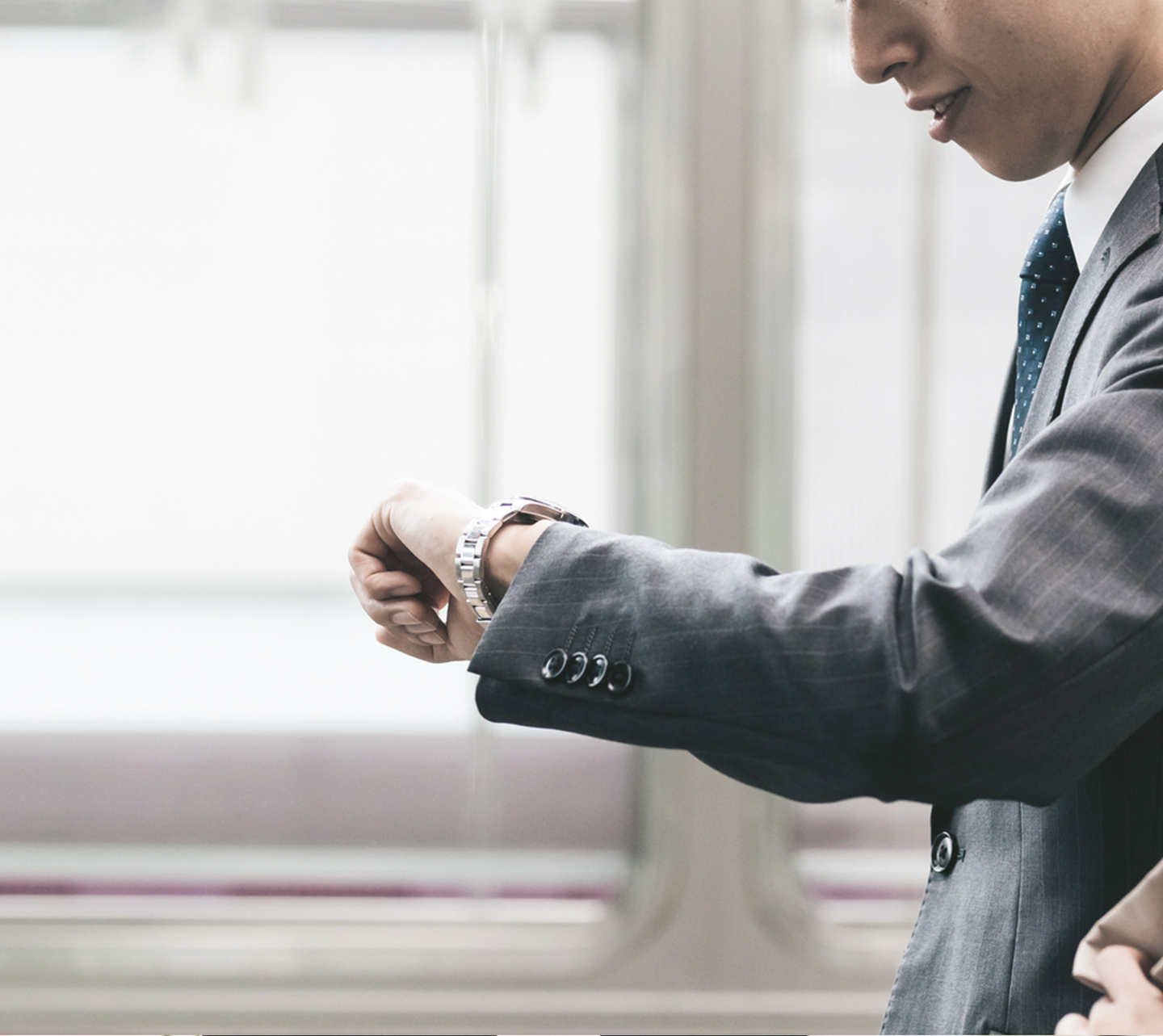 手元の時計を見ながら電車を待つ男性のイメージ画像