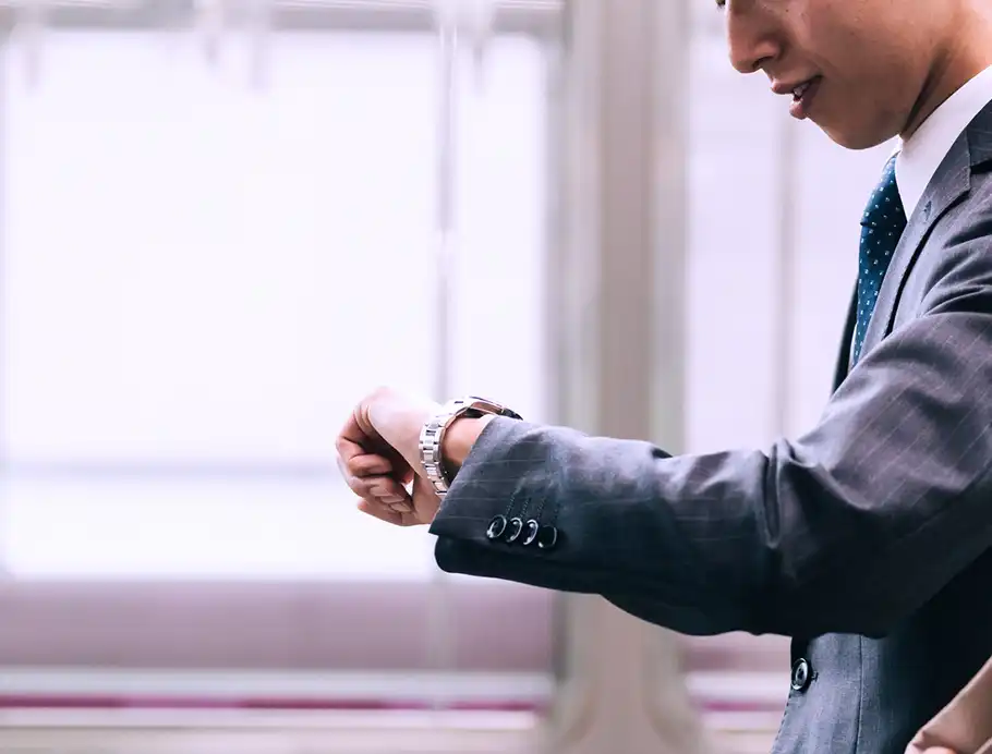 手元の時計を見ながら電車を待つ男性のイメージ画像