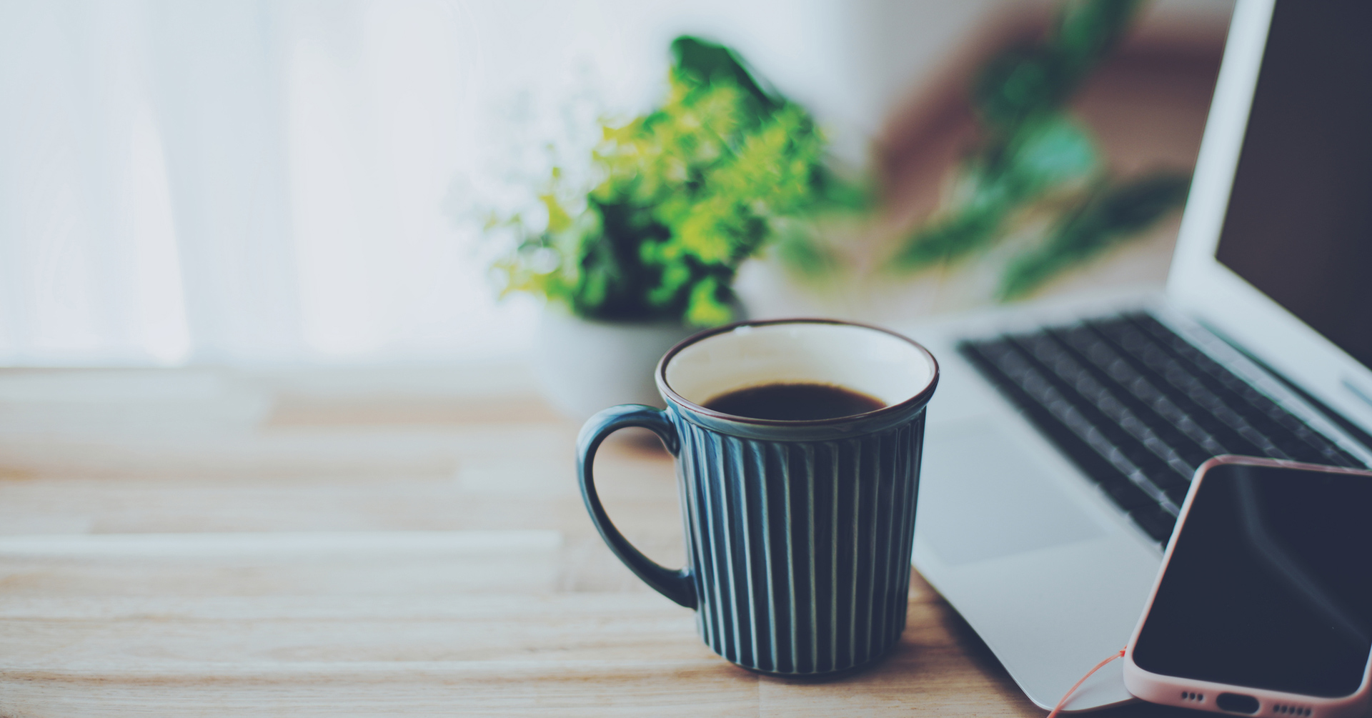 窓辺のテーブルに置かれたノートPCとスマートフォン・コーヒーの室内イメージフォト